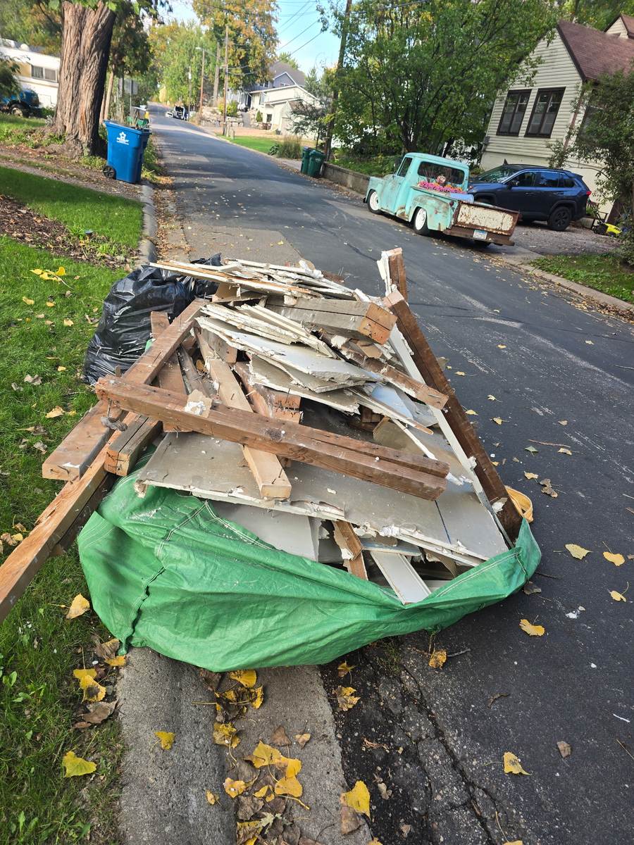 Broken drywall and framing lumber heaped on a Bagster at a residential curb