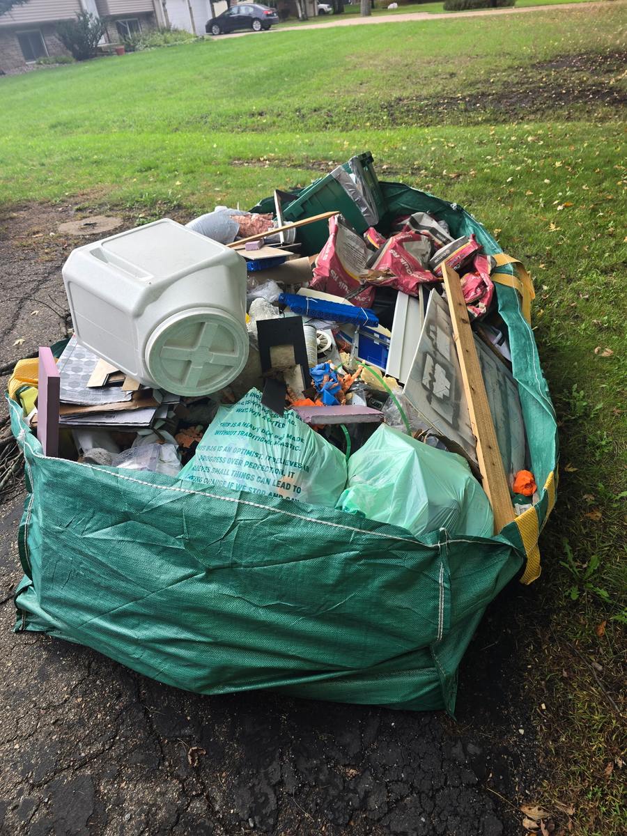 A full Bagster at the curb with a storage bin, tile, mortar bags, wood and trash bags
