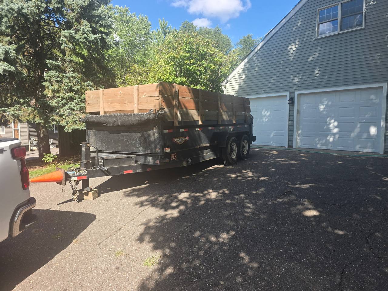PK's black dump trailer with raised wooden sides, parked in a driveway beside a two-car garage
